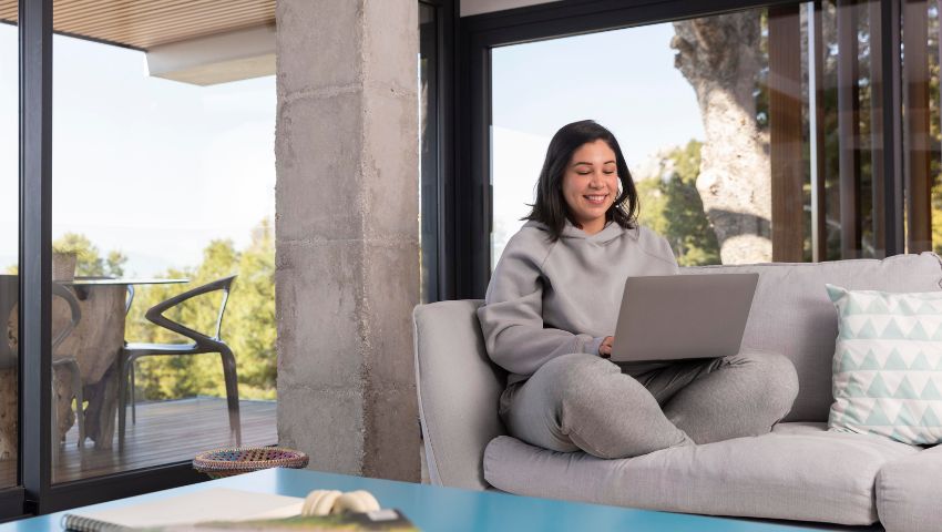 Donna che lavora al laptop in un ambiente luminoso, rappresentando l'importanza di spazi progettati per migliorare produttività e benessere psicofisico.